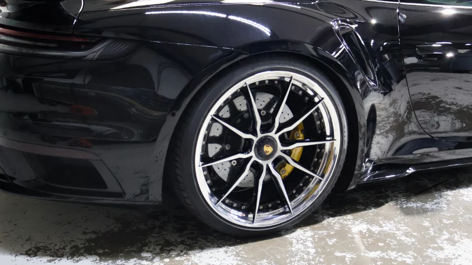 Close-up of the rear wheel of a black Porsche 911, showcasing custom multi-spoke wheels with a polished lip and yellow brake calipers.