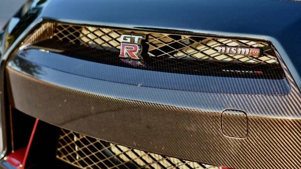 A close-up detail shot of the Nissan GT-R Nismo's carbon fiber front bumper and grille with GT-R and Nismo badges.
