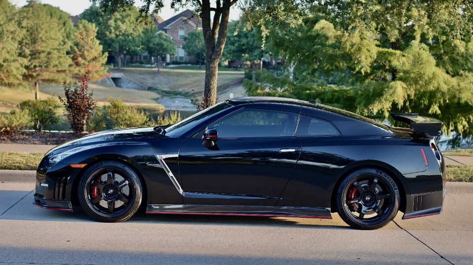 Side profile of a black Nissan GT-R with aftermarket wheels and red brake calipers parked outdoors.