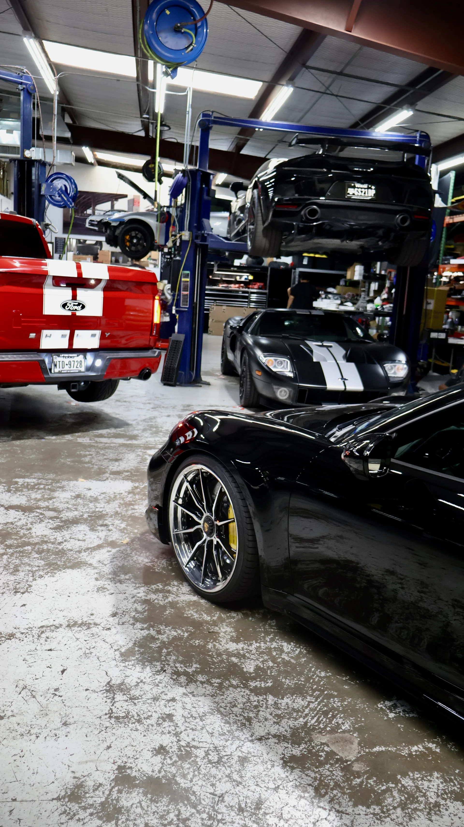 Multiple high-performance cars including a Ford GT, Porsche, and Audi R8 inside a Jotech Motorsports performance tuning shop with car lifts.