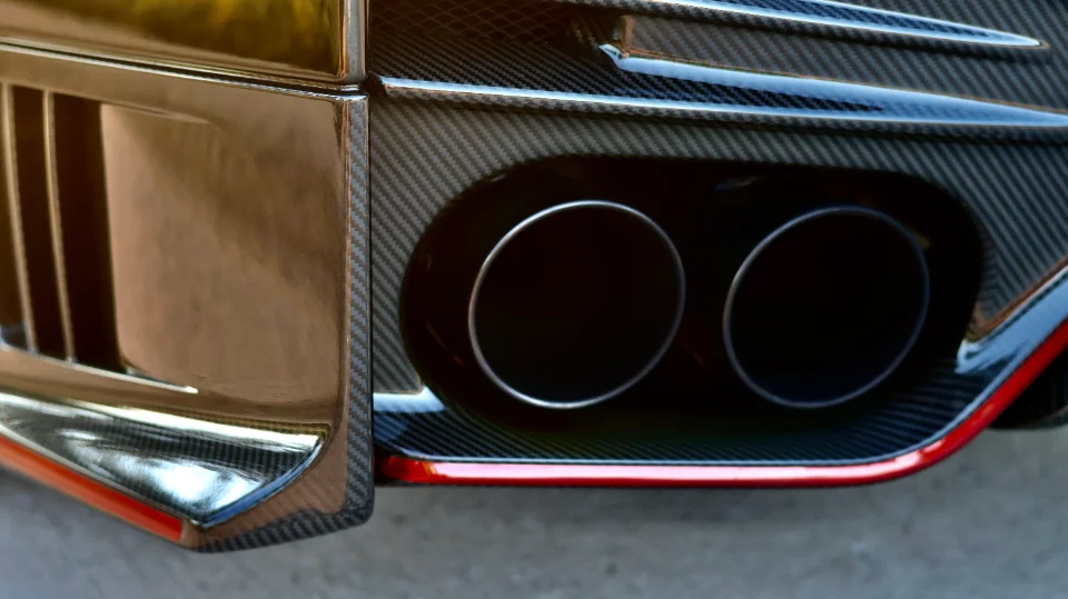 Close-up of a performance car's carbon fiber rear bumper and dual exhaust tips with a red accent.