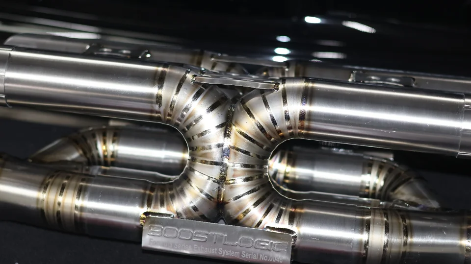 Close-up of a Boost Logic titanium exhaust system with intricate welds and a visible brand plate.