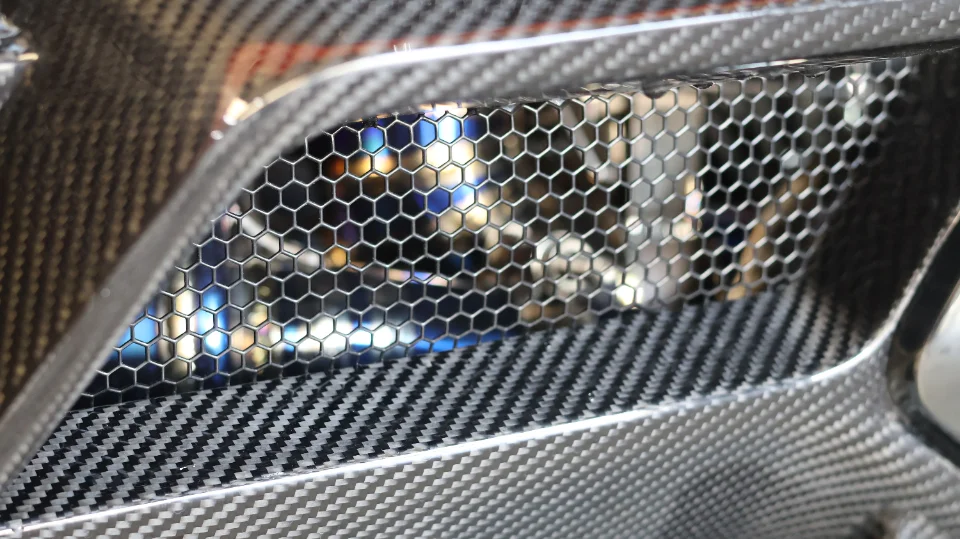 A close-up detail of a carbon fiber automotive vent with a honeycomb mesh grille, showcasing the intricate weave.