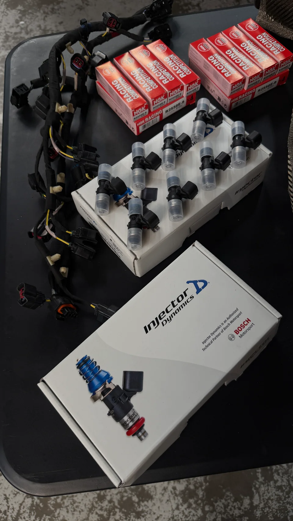 New Injector Dynamics fuel injectors, NGK Racing spark plugs, and a wiring harness laid out on a table.
