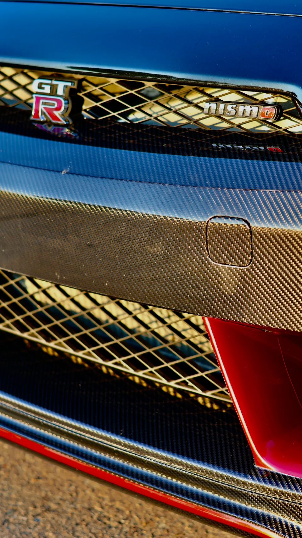 Close-up of the Nissan GT-R Nismo front grille with carbon fiber accents and GT-R badge, showcasing exterior details.