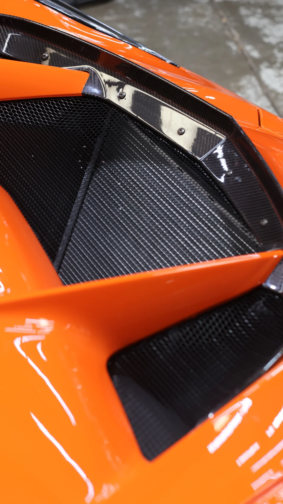 Close-up of an orange supercar's side vent with carbon fiber trim and honeycomb mesh.
