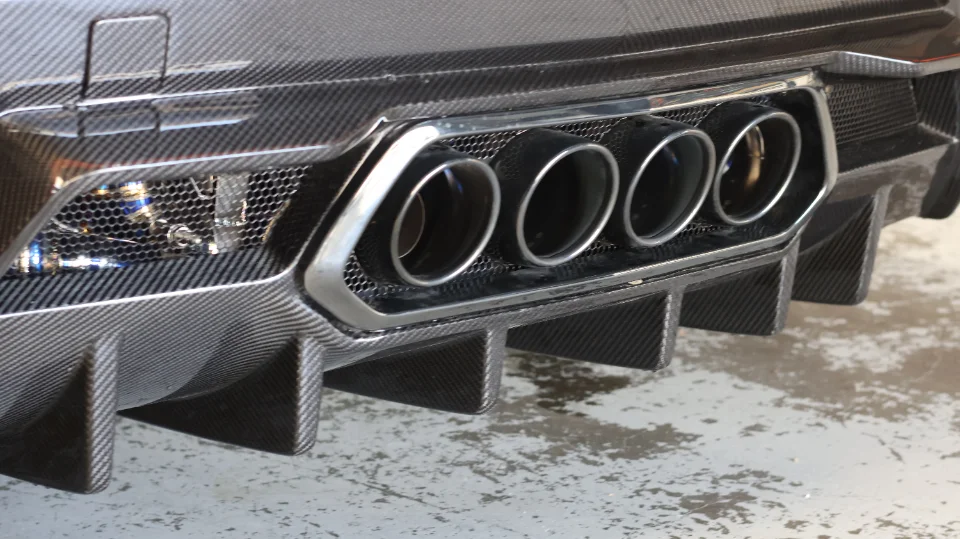Close-up of a car's carbon fiber rear diffuser with integrated quad exhaust tips.