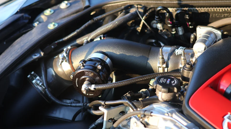 Close-up of a performance engine bay featuring a Tial blow-off valve and aftermarket intake piping.