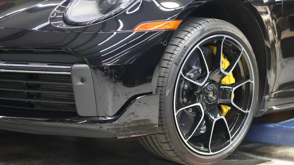 Close-up detail of a black Porsche 911's front wheel, tire, and yellow brake calipers.