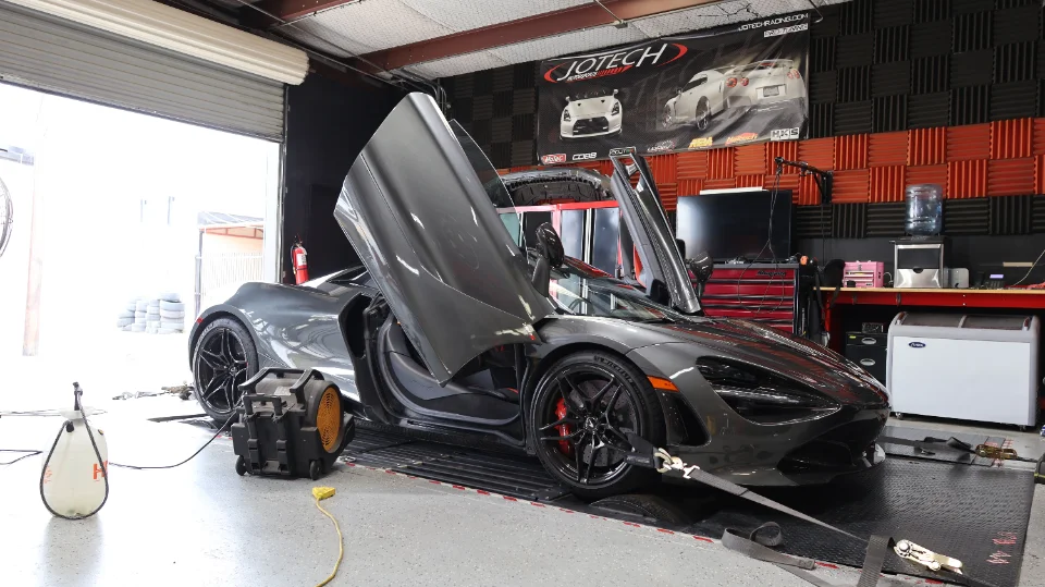 A grey McLaren 720S with its butterfly doors open, strapped to a dynamometer at Jotech Motorsports for performance tuning.