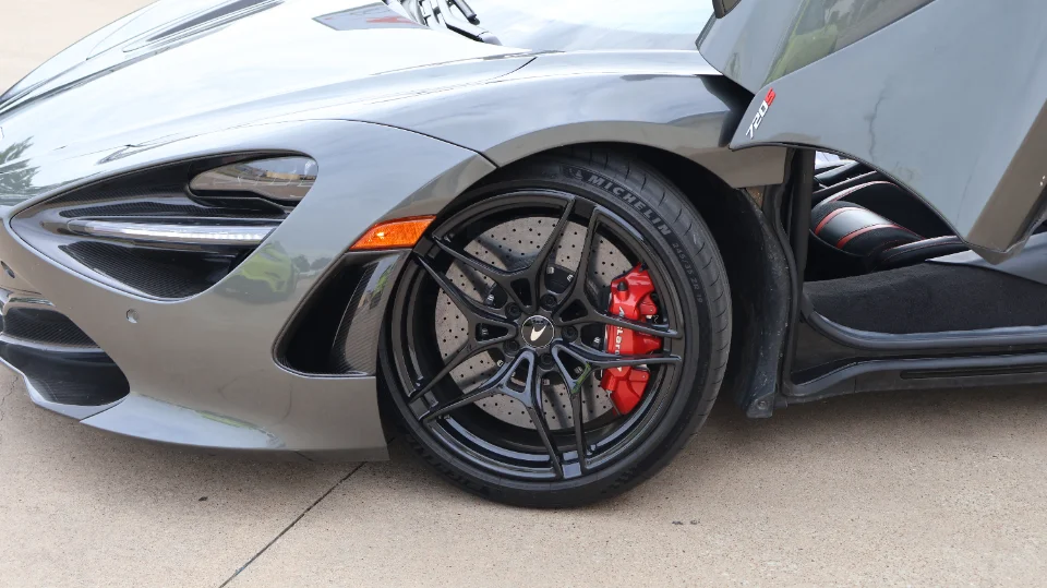 A grey McLaren 720S with black forged wheels and red brake calipers, showcasing the front wheel and fender.