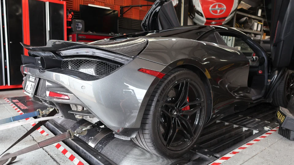 A grey McLaren 720S strapped to a dynamometer at a performance tuning shop, with its doors open.