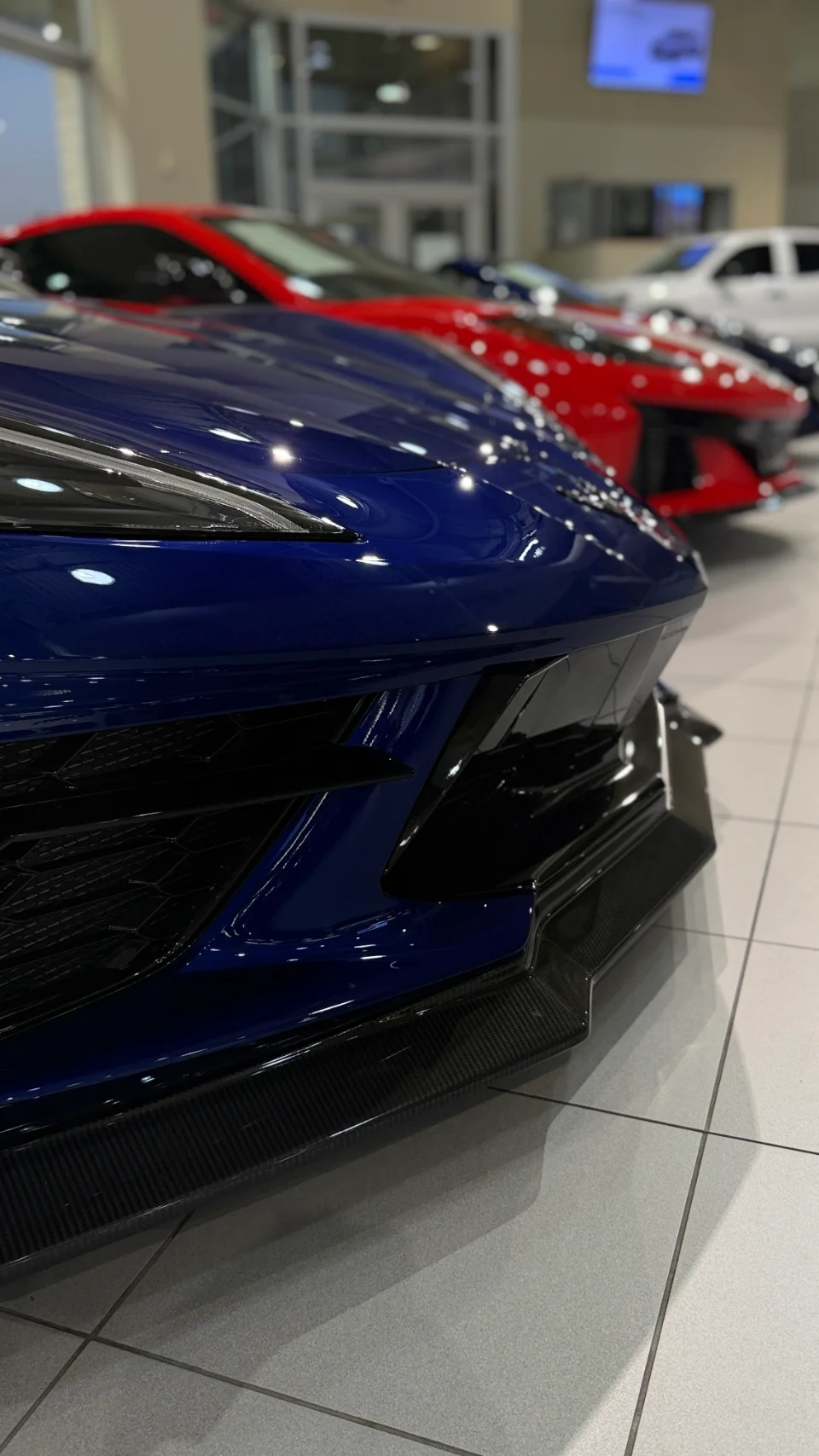 Close-up of a blue Chevrolet Corvette C8 front end with a carbon fiber splitter in a dealership showroom.