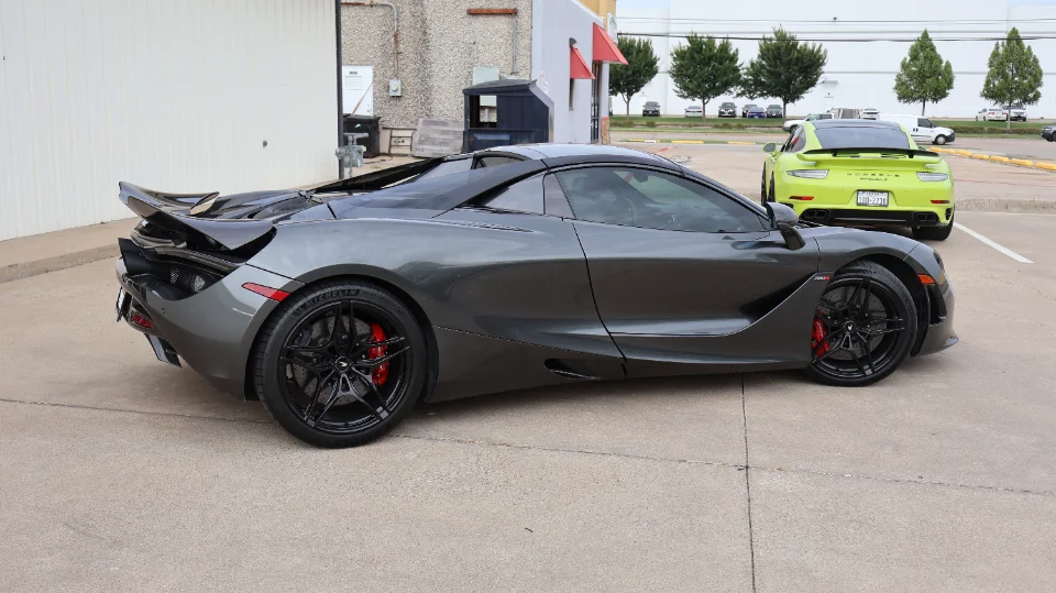 A grey McLaren 720S parked next to a lime green Porsche 911 GT3 RS in a parking lot.
