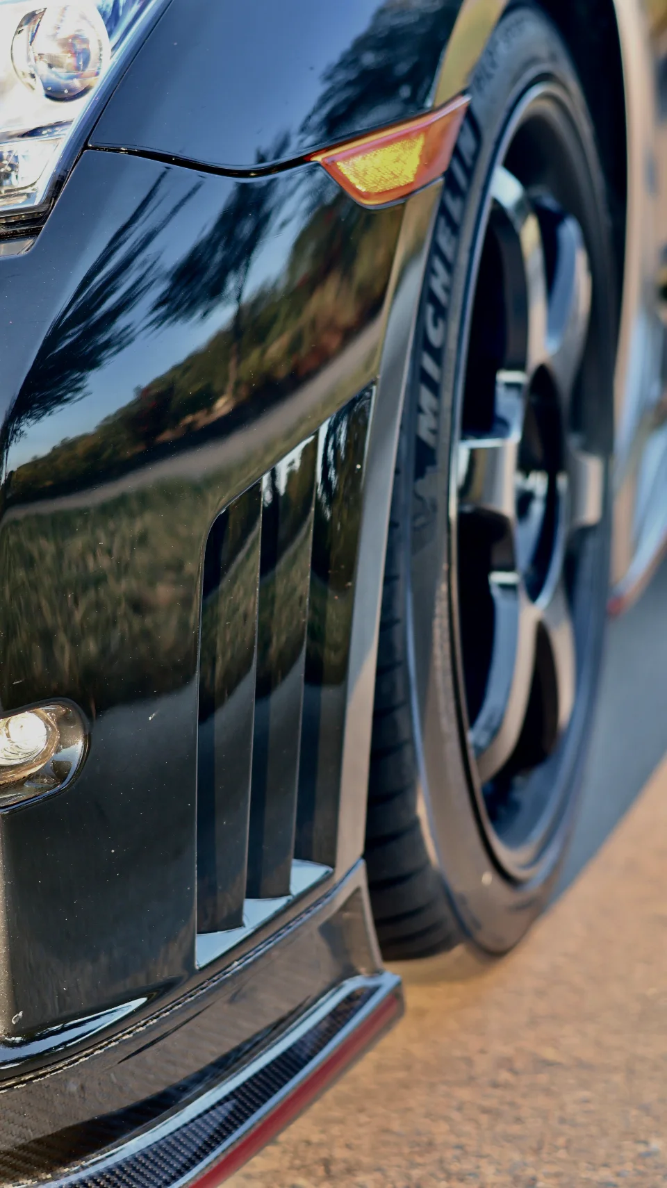 A black Nissan GT-R showing its carbon fiber front splitter, performance wheel, and Michelin tire.