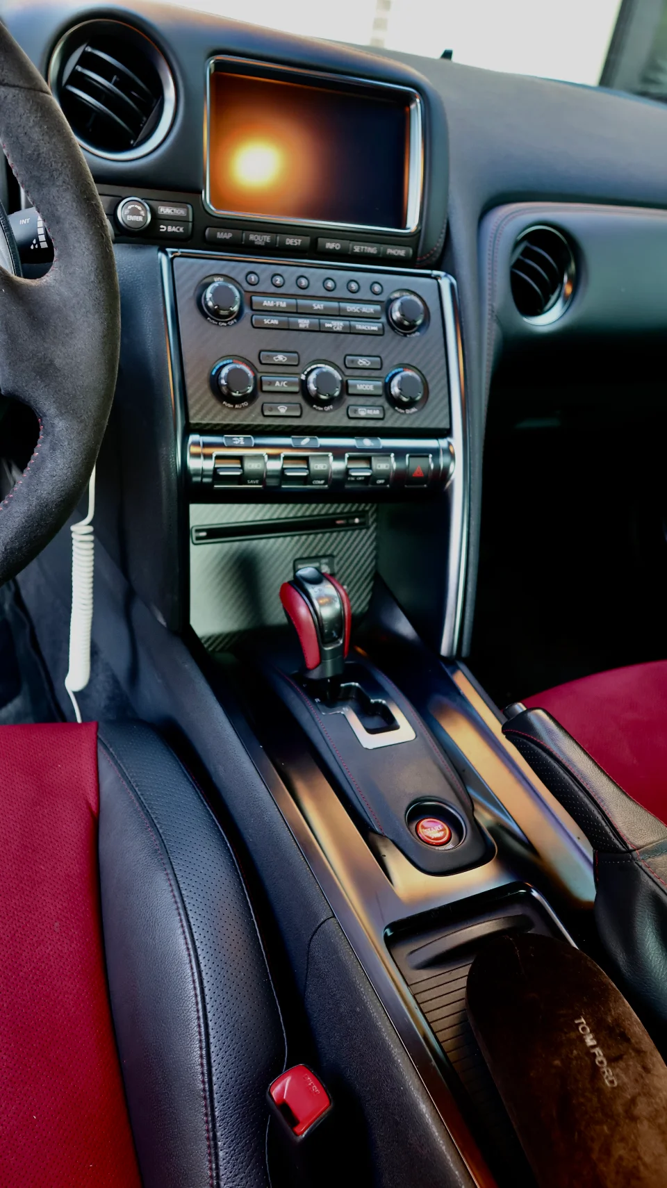 A detailed view of the Nissan GT-R interior, showing the dashboard, carbon fiber center console, red shifter, and red and black seats.