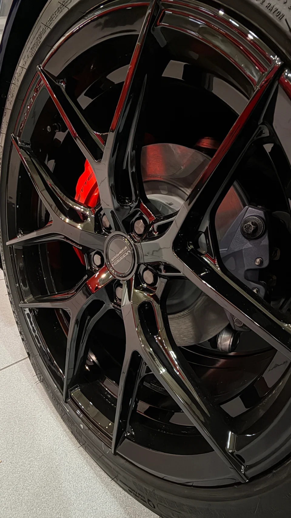 Close-up of a glossy black Vossen wheel with red brake calipers and a tire on a performance car.