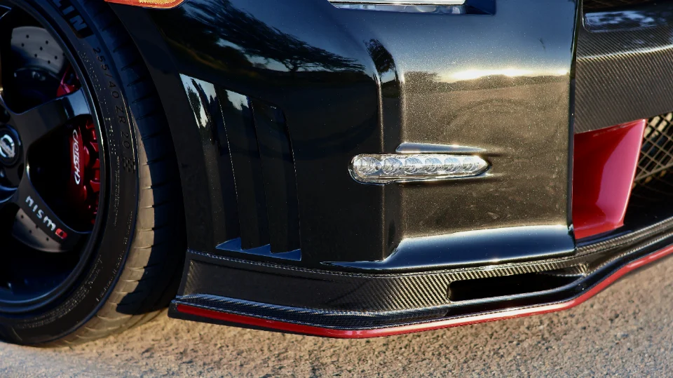 Close-up of a black Nissan GT-R's front bumper featuring a carbon fiber splitter, Nismo wheel, and red brake caliper.