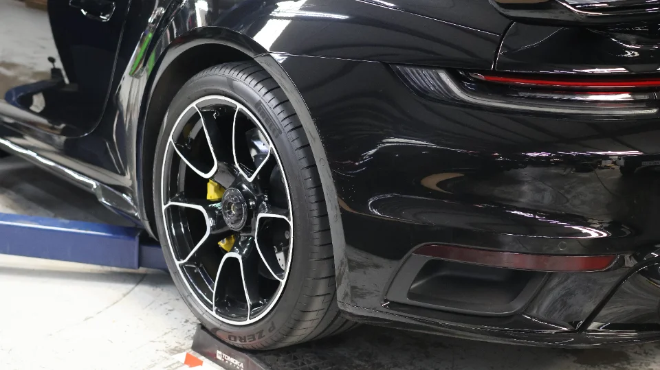A black Porsche 911 on a lift in a shop, showcasing its rear wheel, tire, and yellow brake caliper.