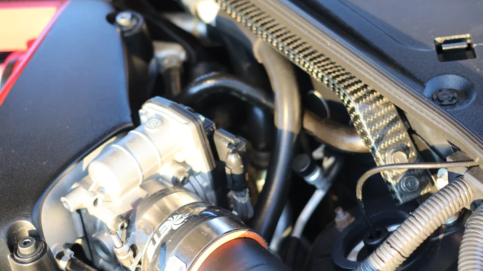 A close-up detail of a car's engine bay showing an aftermarket intake system and carbon fiber components.