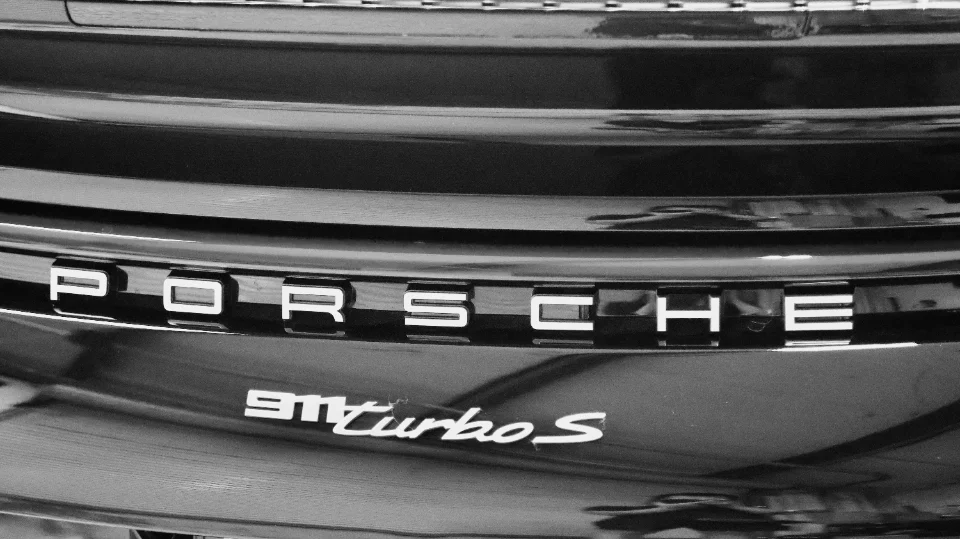 Close-up black and white photo of a Porsche 911 Turbo S rear emblem on a black car.