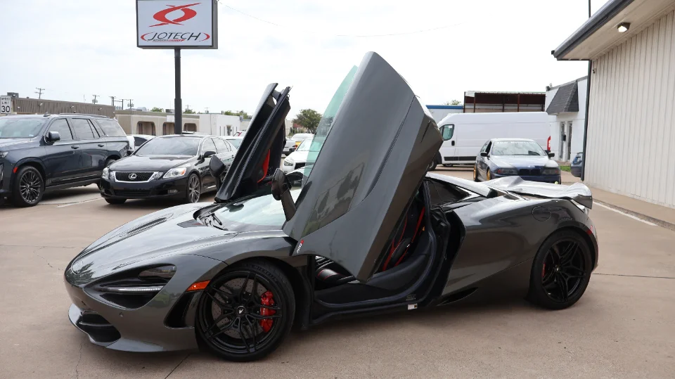 A grey McLaren 720S with its distinctive butterfly doors open, parked outside the Jotech Motorsports facility.