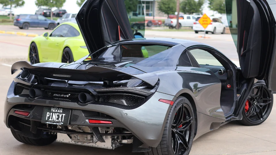 A grey McLaren 720S with its butterfly doors open, showcasing its carbon fiber rear wing and diffuser, parked outdoors.