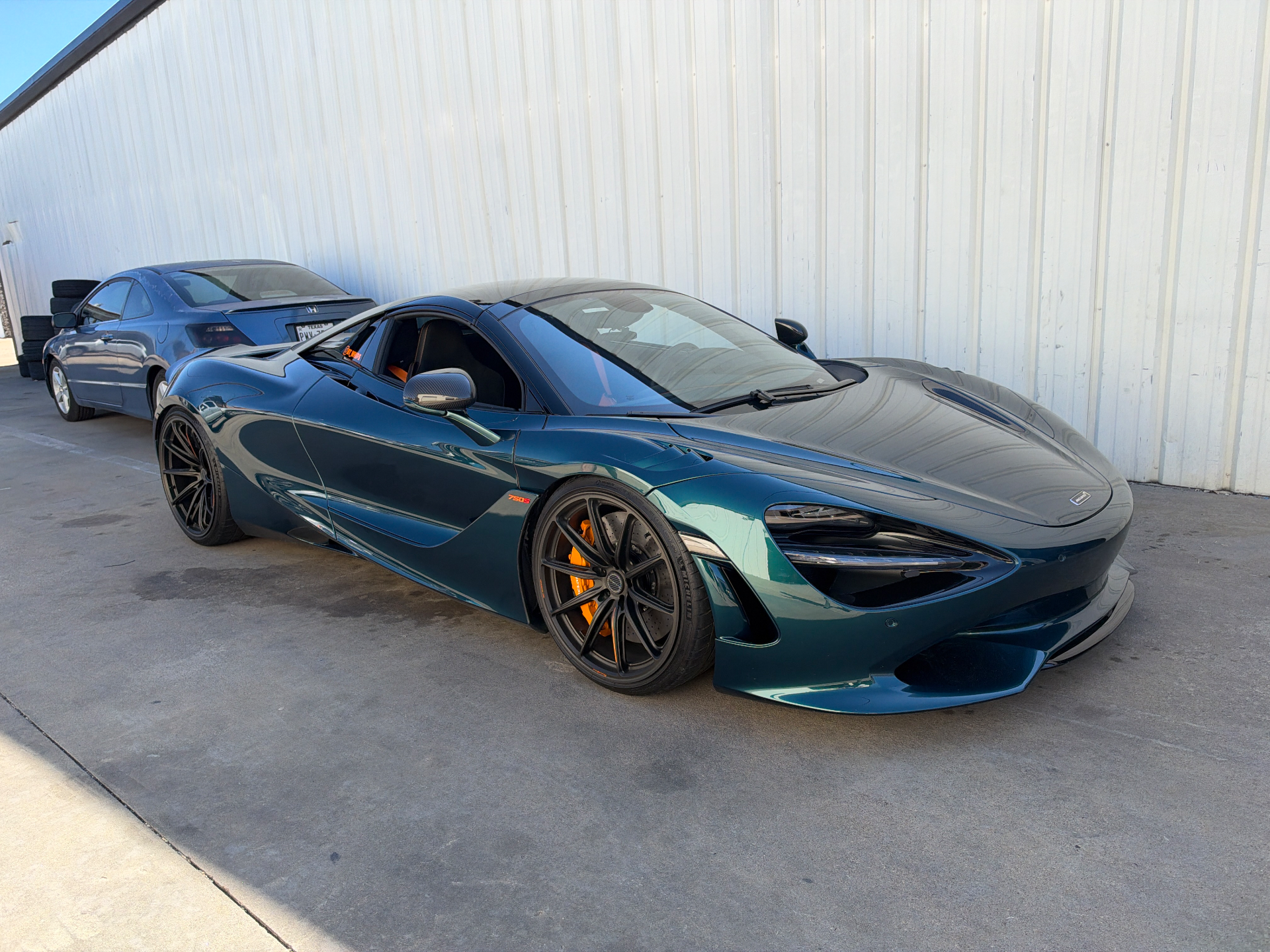 A teal McLaren 720S supercar with orange brake calipers parked outside a building.